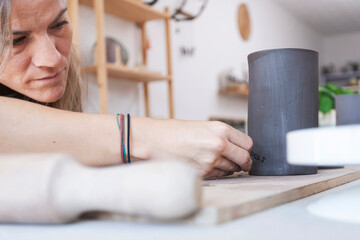 Caucasian woman marking handmade ceramic piece in workshop