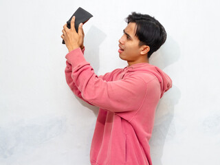 Poor Young Asian man wearing a pink hoodie looking sad and frustrated while holding an empty wallet. Isolated on a white background. Perfect for concepts of poverty or financial struggle
