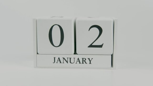 A hand flips a wooden calendar from January 2nd to January 3rd on a white background, marking the passing of time and the start of a new day