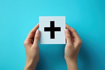Obraz premium two hands holding a white square card with a bold black plus sign on a bright cyan background representing positivity or addition