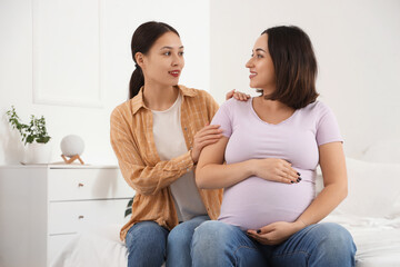 Young Asian doula with pregnant woman sitting in bedroom