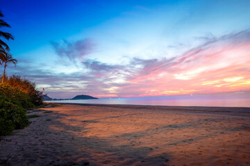 Serene beach at sunset with a vibrant pink and purple sky, calm sea, sandy shore, and distant mountains, ideal for travel and nature themes, amazing waves, and a beautiful light glow.