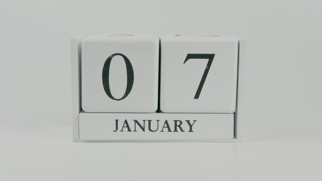 A hand flips a wooden calendar from January 7th to January 8th on a white background, marking the passing of time and the start of a new day