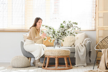 Young woman sitting on sofa with flowering branches in living room