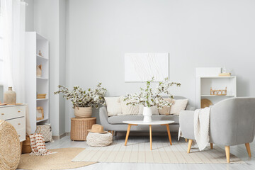 Interior of light living room with sofa, armchair and flowering branches