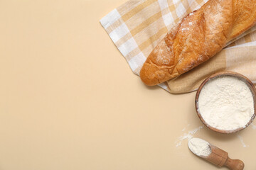 Fresh baguette and wooden bowl of flour on beige background