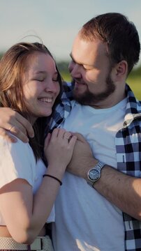 Man and woman are standing in the field and hugging each other filmed in closeup in vertical orientation. Slow motion view of happy Caucasian couple having date on nature and kissing at summer day