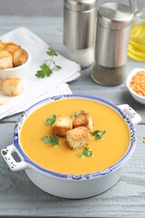 Delicious lentil cream soup served with croutons on grey wooden table, closeup