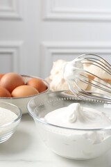 Whisk with whipped cream and other ingredients on light table, closeup. Cooking meringue cookies