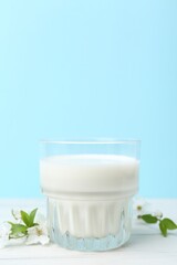 Glass of fresh milk on white wooden table against light blue background. Space for text