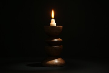 Burning candle in candlestick on black background