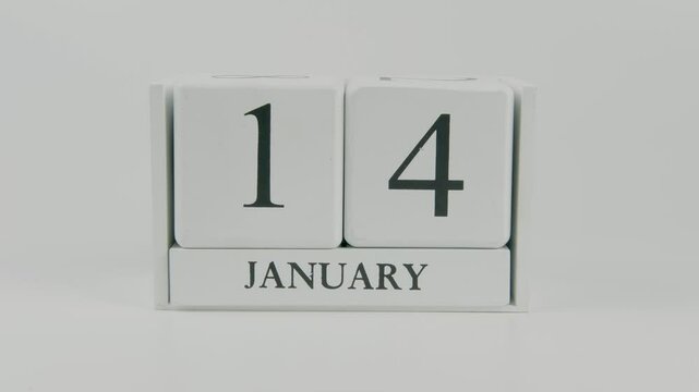 A hand flips a wooden calendar from January 14th to January 15th on a white background, marking the passing of time and the start of a new day