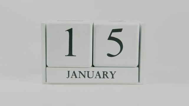A hand flips a wooden calendar from January 15th to January 16th on a white background, marking the passing of time and the start of a new day