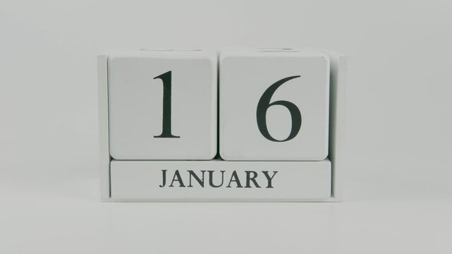 A hand flips a wooden calendar from January 16th to January 17th on a white background, marking the passing of time and the start of a new day