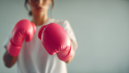 Female boxer wearing pink gloves punching toward the camera against a clean neutral background. Action sports, fitness, martial arts, strength, breast cancer awareness. Image with copy space
