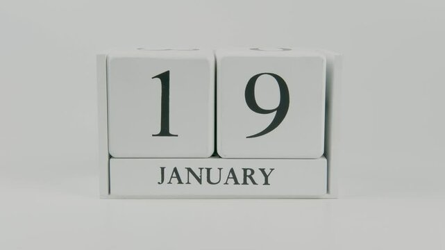 A hand flips a wooden calendar from January 19th to January 20th on a white background, marking the passing of time and the start of a new day