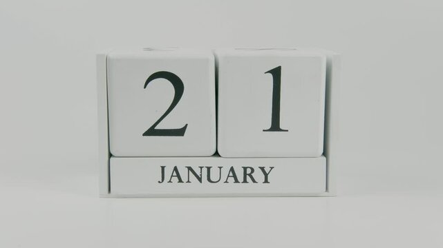 A hand flips a wooden calendar from January 21st to January 22nd on a white background, marking the passing of time and the start of a new day
