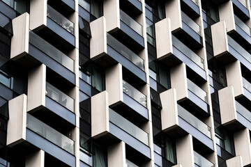 Layered geometric facade of modern building with alternating white and dark elements, creating rhythm, pattern and structural contrast through architectural repetition.