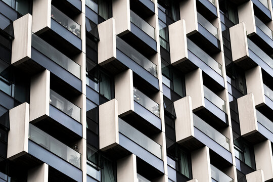 Layered geometric facade of modern building with alternating white and dark elements, creating rhythm, pattern and structural contrast through architectural repetition.