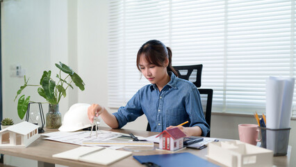 Fototapeta premium Asian Woman Architect Creating Blueprint Plan Design Asian Woman Architect Focusing Blueprint Plan Design on Her Desk in Office 137