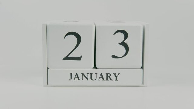 A hand flips a wooden calendar from January 23rd to January 24th on a white background, marking the passing of time and the start of a new day