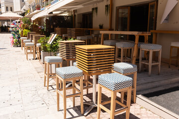 Modern Bar Terrace with High Stools. Stylish outdoor bar area with wooden high tables and patterned stools along a sunny Zakynthos street.