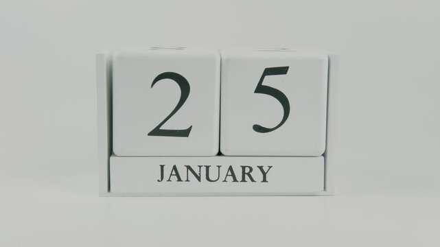 A hand flips a wooden calendar from January 25th to January 26th on a white background, marking the passing of time and the start of a new day