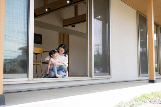 軒先や縁側で抱っこでくつろぐ母親と娘（子供）子育ての幸せのイメージ広角の全身