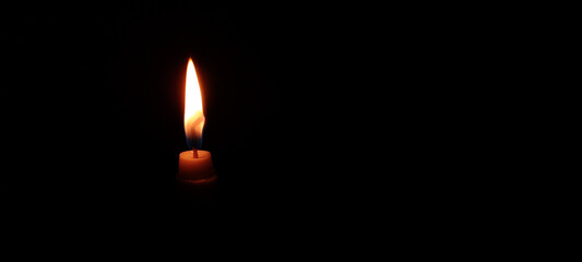 A bright yellow flame dances atop a burning wax candle in the dark black night, radiating a warm, romantic candlelight