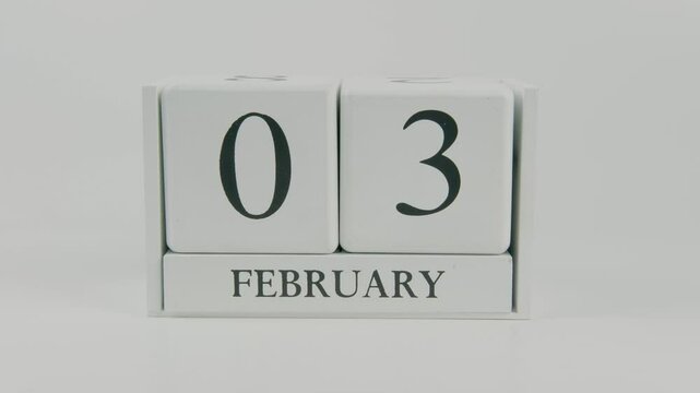A hand flips a wooden calendar from February 3rd to February 4th on a white background, marking the passing of time and the start of a new day