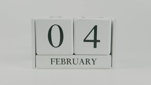 A hand flips a wooden calendar from February 4th to February 5th on a white background, marking the passing of time and the start of a new day