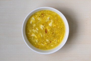 Delicious healthy corn soup cooked with egg, served in a white bowl on a wooden background. Top view.
