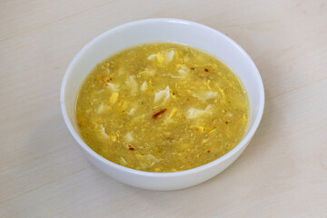 Delicious, healthy corn soup with egg, served in a white bowl on a wooden table.
