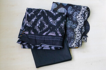 Folded embroidered beautiful black cotton salwar kameez three-piece set for women, on a light wooden background.