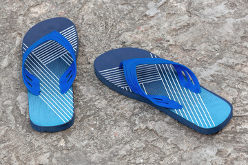 A pair of stylish navy blue flip-flops on a concrete floor. These light, sandal-like shoes are...