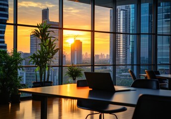 Modern office space with city views at sunset. A laptop sits on a wooden table, with plants in the foreground and a panoramic view of the cityscape at golden hour