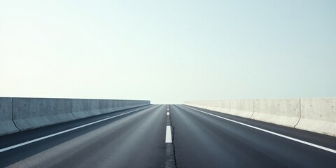Fototapeta premium Endless Highway A Straight Asphalt Road with Concrete Barriers Under a Pale Sky