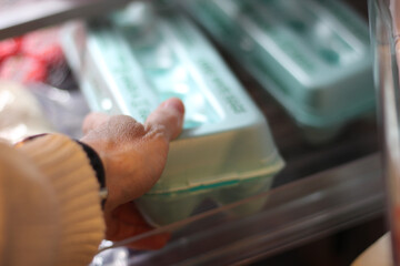 a person reaching for an egg carton in a home refrigerator with bokeh light effect lifestyles design element