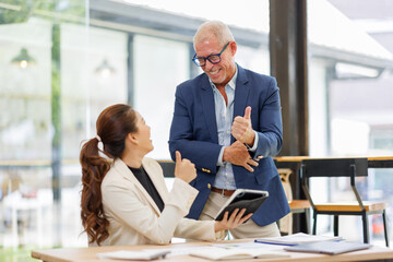 Two business people, a business man and a business woman, engage in a discussion as they read a financial report together. asian business professionals working together in a modern finance company.