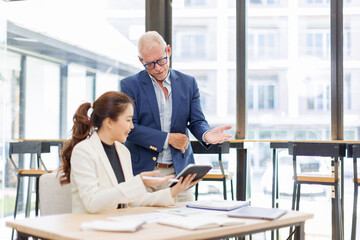 Two business people, a business man and a business woman, engage in a discussion as they read a financial report together. asian business professionals working together in a modern finance company.