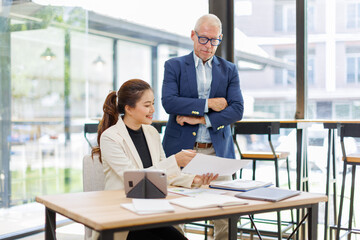 Two business people, a business man and a business woman, engage in a discussion as they read a financial report together. asian business professionals working together in a modern finance company.