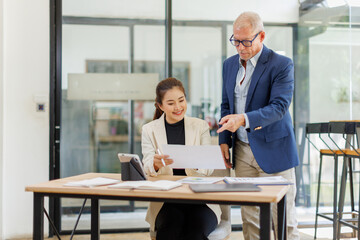 Two business people, a business man and a business woman, engage in a discussion as they read a financial report together. asian business professionals working together in a modern finance company.
