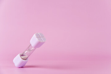 Little white hourglass falling on a soft pink backdrop