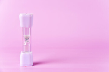 Pastel pink sand timer against a matching background, symbolizing the passage of time. White hourglass with copy space