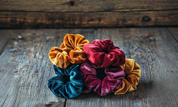 A vibrant collection of velvet scrunchies in rich autumn colors, artistically arranged on a rustic wooden surface, evoking a cozy, seasonal atmosphere