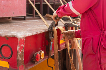 Action of a worker is tightening latching strap belt to secure the load object on trailer truck....
