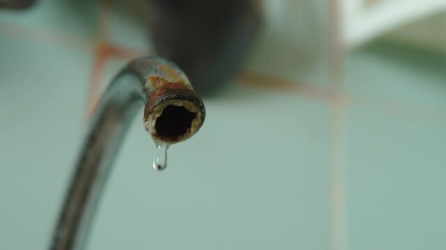 Water drops drip rhythmically from rusty tap spout close up. Increased water consumption and risk of drinking water contamination due to malfunction. Poor condition of kitchen equipment.