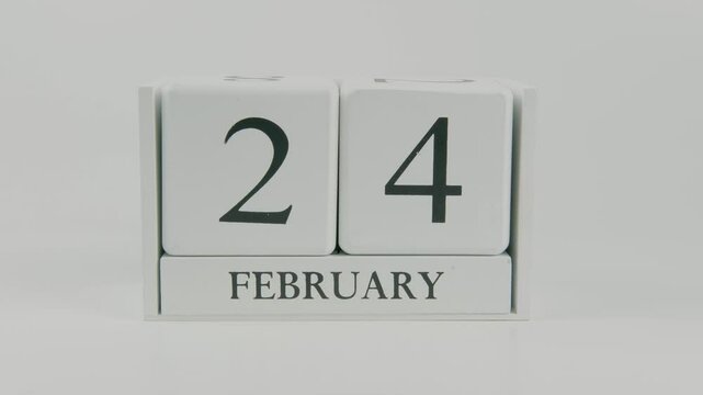 A hand flips a wooden calendar from February 24th to February 25th on a white background, marking the passing of time and the start of a new day