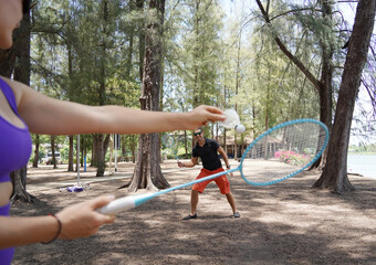 A man and a young woman are playing badminton together in a park