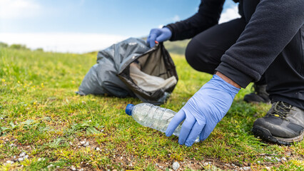 Volunteer man in blue gloves picking up garbage from the field and putting it in garbage bags.